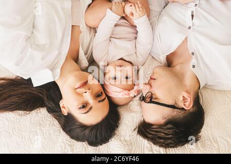 Glücklicher junger Vater, Mutter und niedliches Baby Mädchen liegen auf hellem Bett. Draufsicht. Stockfoto