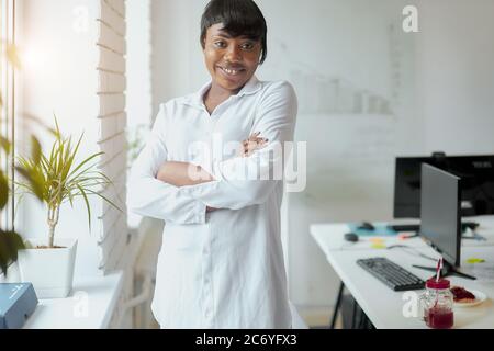 Porträt der hübschen afroamerikanischen Geschäftsfrau trägt weißes Hemd im Büro stehen neben Fenster posiert. Business People Konzept Stockfoto