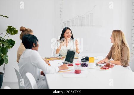 Junge Business-Damen interagieren während Kaffeepause bei der Business-Konferenz im weißen Büro, Obst und Tasse Tee auf dem Tisch. Frauen Kollegen versammelt Stockfoto