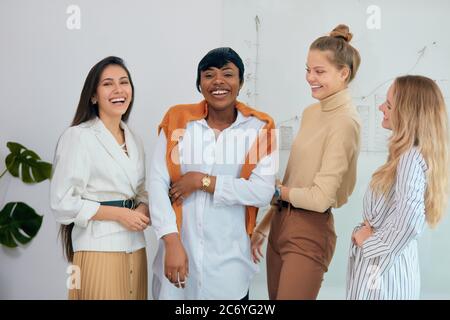 Gruppe von jungen, vielfältigen multiethnischen Team Blick auf Kamera, posieren und lächeln. In legerer Kleidung, kaukasische und afrikanische Damen im weißen Büro Stockfoto