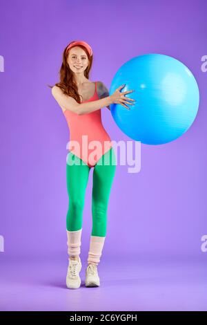 Volle Länge vertikale Schuss von sportlichen niedlichen Ingwer Mädchen macht Übungen mit blauen Fitness-Ball, so dass Aufwärmen trainieren, Training Brustmuse und Hand m Stockfoto