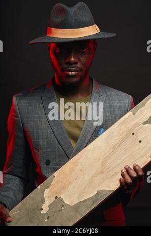 Portrait von energischen, sportlichen, selbstbewussten schönen afrikanischen Mann infashionable Blazer Anzug hält Longboard in den Händen, posiert isoliert im Studio auf da Stockfoto