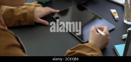 Ausschnittaufnahme der weiblichen Designerzeichnung auf einem digitalen Tablet mit Stylus-Stift auf dem Schreibtisch mit Malwerkzeugen Stockfoto