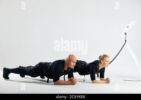 Mann und Frau in elektrischen Muskelstimulation Anzüge tun Plank Übung. Voller Länge Foto. Isoliert weißen Hintergrund. Hobby, Lebensstil Stockfoto