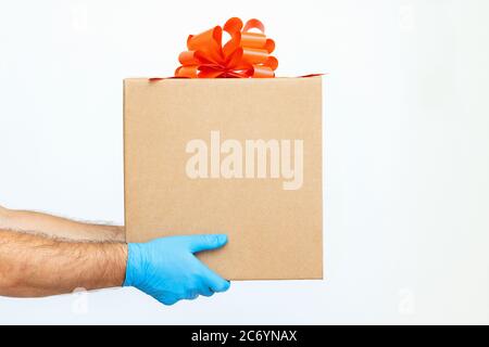 Ein Mann in medizinischen Handschuhen hält eine Schachtel mit einem roten Band und einer Schleife auf weißem Hintergrund. Verkauf. Geschenk. Coronavirus, Quarantäne, Verkauf Stockfoto