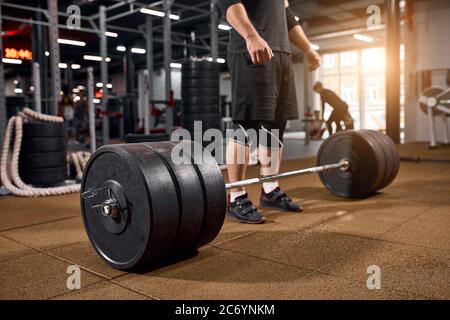 Schwere schöne Langhantel auf dem Boden des Fitnessraums, männliche Beine stehen in der Nähe Bar, Bodybuilder üben für das Training, aktive Menschen, professionelle Sportkonzept Stockfoto