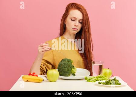 Symptome der Anorexie manifestiert sich in Abneigung gegen Nahrung. Portrait der Grimacing unzufrieden Gesichtsemotionsdruck Dame weigert sich, frische grüne sa essen Stockfoto