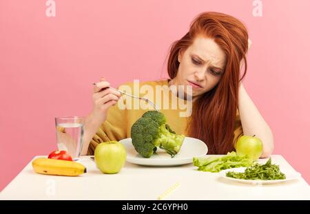 Studio Portrait von verärgert betont stumpf Unzufriedenheit unzufrieden unzufrieden rothaarige Frau hält Gabel in der Hand Blick auf frischen Brokkoli, als ob es s Stockfoto