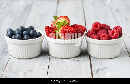 Sortierte frische saftige Beeren in drei kleinen Schalen, Blaubeere, Erdbeere und Himbeere Stockfoto