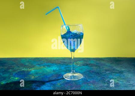 Blauer Cocktail in Weinglas mit Spritzer auf gelbem und blauem Hintergrund. Stockfoto