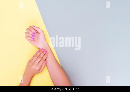 Helle trendige weibliche Maniküre. Frauenhand mit rosa und violetter Maniküre auf gelbem und blauem Hintergrund. Stockfoto