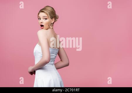 Schockiert Braut in weißen Hochzeitskleid Blick auf Kamera isoliert auf rosa Stockfoto
