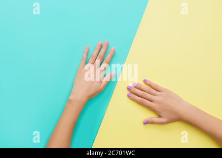 Helle trendige weibliche Maniküre. Frauenhände mit orange und violett Maniküre auf gelb und türkis Hintergrund. Stockfoto