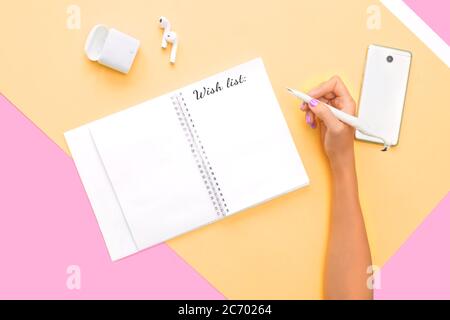 Wunschliste Schriftzug in Hinweis, Blogger Konzept. Draufsicht auf Kopfhörer, Telefon und Notebook mit Hand mit perfekter heller Maniküre auf orange rosa Rückenfarbe Stockfoto