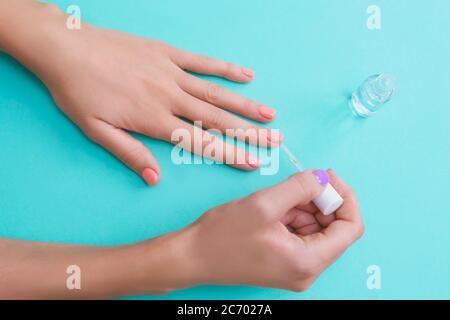 Flach legen Hände und klare Politur. Das Mädchen malt ihre Nägel auf einen türkisfarbenen Hintergrund. Stockfoto