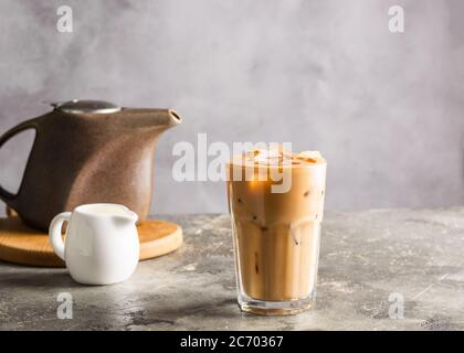 Kalter schwarzer Kaffee mit Eiswürfeln und Milch im hohen Glas. Erfrischendes Kaffeegetränk auf dem grauen Hintergrund des Tisches. Nahaufnahme Stockfoto
