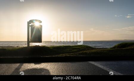 Horizontales Landschaftsfoto von Mülltonnen an einem Strand von Auckland mit einem Sonnensterben, der durch den Papierkorb scheint Stockfoto