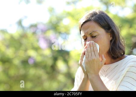 Kranke Erwachsene Frau, die Nase bläst, mit Gewebe, das im Sommer im Park steht Stockfoto