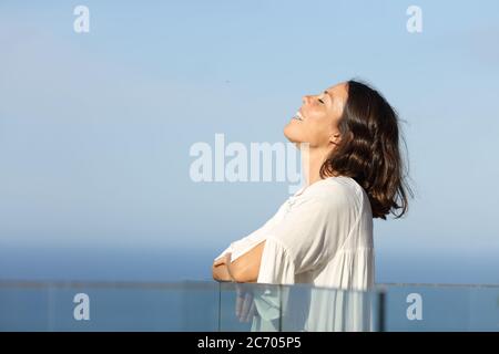 Glückliche Erwachsene Frau atmen frische Luft am Strand stehend auf einem Balkon Stockfoto