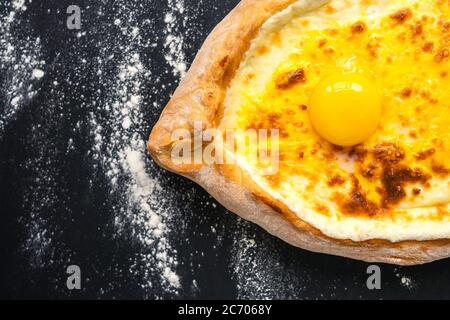 Khachapuri adjara traditionelle georgische Küche Mahlzeit aus der Nähe. Gebackenes Brot als Boot mit Käse und Eierfüllung auf schwarzem Hintergrund, verziert mit flou Stockfoto