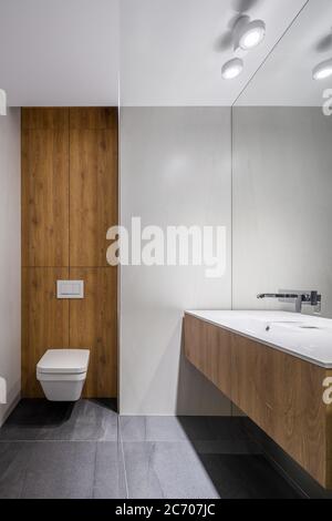 Weißes Badezimmer mit modernen Holzdetails an Wänden und Schubladen sowie klassisch weißer Toilette und Waschbecken Stockfoto