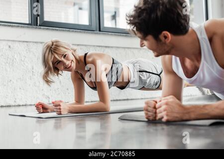 Selektive Fokus der glücklichen Sportlerin dabei Plank und Blick auf den Mann im Fitnessstudio Stockfoto