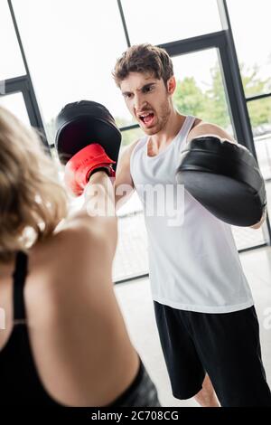 Selektive Fokus des Mannes in Boxpads schreien in der Nähe Mädchen Training im Sportzentrum Stockfoto