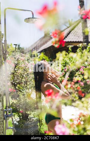 Frau Duschen ausserhalb in tropischen Grün Bali Garten mit vielen Blumen. Frische Spritzer auf sauberes Wasser. Luxus Spa Stockfoto
