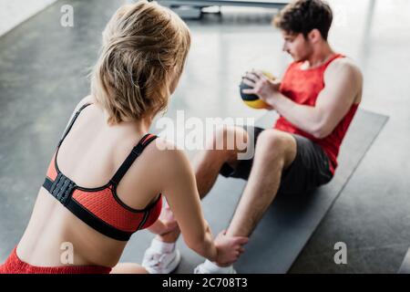 Selektive Fokus der sportlichen Mädchen hält Beine des Sportlers mit Ball auf Fitness-Matte trainieren Stockfoto