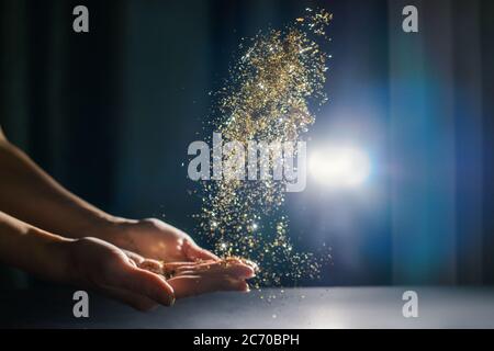 Hände mit fliegenden Pailletten und funkelt. Licht auf Hintergrund. Festliches Konzept. Stockfoto