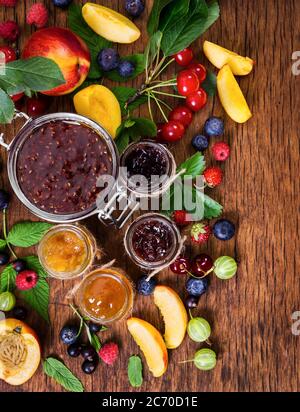 Marmelade aus verschiedenen Beeren in Gläsern auf rustikalem Holzhintergrund. Stockfoto