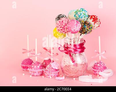 Cake Pops mit rosa Verzierung und Dekoration auf Papier Form und bunte Cake Pops in Glasvase auf rosa Hintergrund Stockfoto