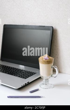 Dalgona Kaffee in einer klaren Tasse, Notizblock, Stift und Computer auf dem Tisch. Draufsicht. Kaffeepause am Arbeitsplatz eines Bloggers oder Freiberuflers Stockfoto