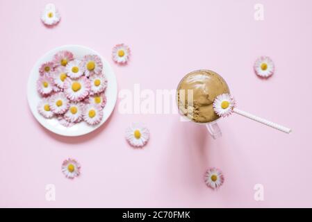 Dalgona Kaffee in einer transparenten Tasse mit einem Papierrohr, ein Teller mit Blumen Gänseblümchen. Draufsicht Stockfoto