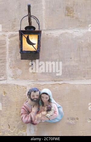 Heilige Familienstatue unter einer Laterne auf einer Texturwand eines Hauses, Vittoriosa (Birgu), Malta Stockfoto