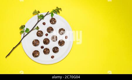 Protein Erdnussbutter Energie Bisse oder Energiebälle. Hausgemachte rohe Schokoladentrüffel mit Nüssen und in Kokosflocken auf Teller und gelbem Hintergrund. Stockfoto