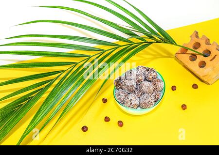 Protein Erdnussbutter Energie Bisse oder Energiebälle. Hausgemachte rohe Schokoladentrüffel mit Nüssen auf Teller mit Palmblatt auf gelbem Hintergrund. Stockfoto