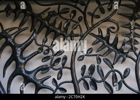 Ein Metallgrill in Form eines Baumzweiges mit schwarzen Blättern auf hellgrauem Hintergrund. Ursprünglicher Hintergrund für den Kopierbereich. Stockfoto