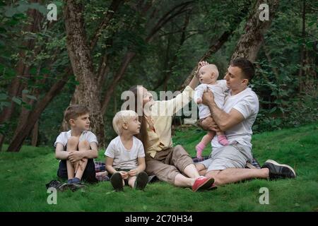 Familienpicknick im Freien. Große Familie. Mama Papa und drei Kinder sitzen auf Gras Stockfoto