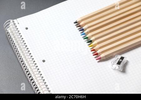 Flache Ansicht von weißem Notizbuch, Farbstifte und Bleistiftspitzer auf einem Tisch. Vorbereitung auf eine Schule. Zurück zur Schule. Stockfoto