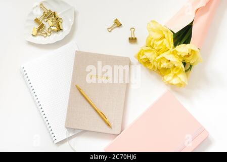 Frühling feminine Arbeitsbereich Blogger. Notizbücher mit einem Stift, ein Strauß gelber Tulpen auf weißem Hintergrund. Modisch-stylischer Flachlappen Stockfoto