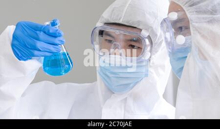 Covid-19-Tests im Labor. Zwei Wissenschaftler diskutieren über die blaue Flüssigchemikalie im Erlenmeyerkolben. Gesundheitswesen und medizinisches Konzept. Stockfoto