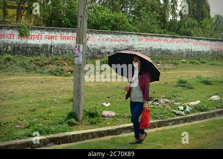 Eine Frau mit Gesichtsmaske, die einen Regenschirm trägt, während sie an einem Straßenrand in der Provinz Bagmati Pradesh in Nepal geht. Stockfoto