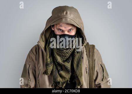 Dunkle Foto von Young Handsome Mann trägt schwarze protaktive Gesichtsmaske und Jacke mit Kapuze auf grauem Hintergrund isoliert Stockfoto