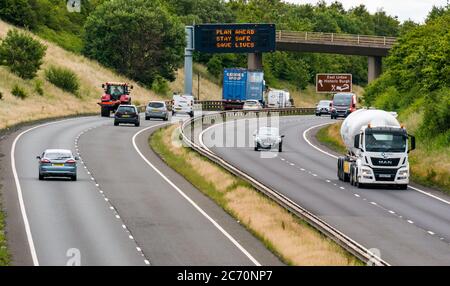 East Lothian, Schottland, Großbritannien, 13. Juli 2020. A1 Covid-19 Reiseberatung Schottland geht in Phase 3 auf einer Überfahrbrücke mit der neuen Iteration der Botschaft: 'Plan ahead, Stay Safe, Save Lives'. Dies ist die vierte Iteration der Coronavirus-Slogans, die von der schottischen Regierung während der Pandemie verwendet wurden. Die zweispurige Straße ist viel geschäftiger und fast wieder auf normale Verkehrsniveaus Stockfoto