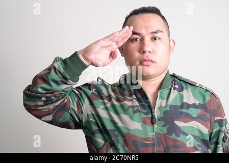 Junge gut aussehende übergewichtige asiatische Mann in militärischen Uniform salutieren Stockfoto