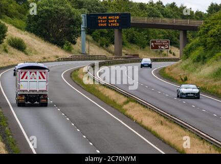 East Lothian, Schottland, Großbritannien, 13. Juli 2020. A1 Covid-19 Reiseberatung Schottland geht in Phase 3 auf einer Überfahrbrücke mit der neuen Iteration der Botschaft: 'Plan ahead, Stay Safe, Save Lives'. Dies ist die vierte Iteration der Coronavirus-Slogans, die von der schottischen Regierung während der Pandemie verwendet wurden. Die zweispurige Straße ist viel geschäftiger und fast wieder auf normale Verkehrsniveaus Stockfoto