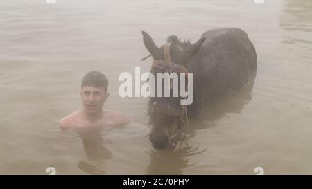 Guroymak, Bitlis, Türkei - Februar 2020: Kleiner Junge und sein Pferd im Thermalwasser, Freundschaft mit Haustieren, Tierdusche Stockfoto