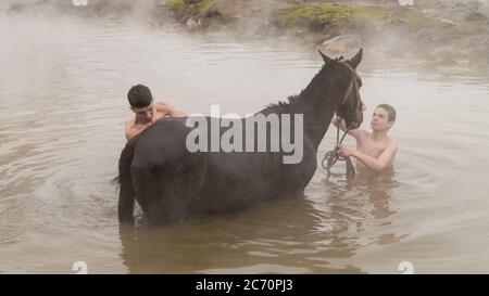 Guroymak, Bitlis, Türkei - Februar 2020: Jungen waschen ihr Pferd im Thermalwasser, Konzept der Freundschaft mit Haustieren, Tierdusche Stockfoto