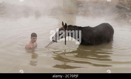 Guroymak, Bitlis, Türkei - Februar 2020: Kleiner Junge und sein Pferd im Thermalwasser, Freundschaft mit Haustieren, Tierdusche Stockfoto